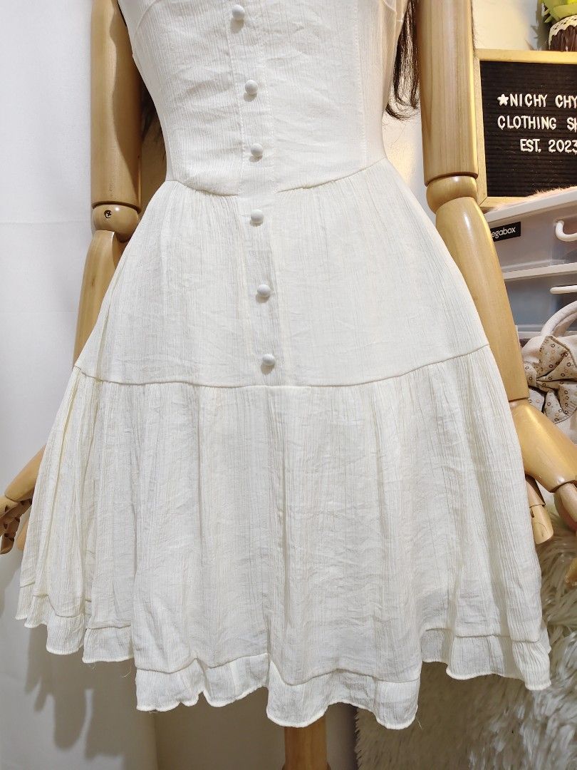 White Corset Style Mini Dress (Category: Dresses) located in Manila. Submitted by chynii_28 (Listing ID 1467624811, Image 3). Description: - Style: White sleeveless mini dress with button-up front detailing - Neckline & Fit: Square neckline and fitted bodice with a flared tiered skirt - Fabric: Lightweight, textured fabric with subtle vertical stripes - Measurements: Bust 32/46", Waist 26/30", Length 32" - Perfect for: Sunny days, casual hangouts