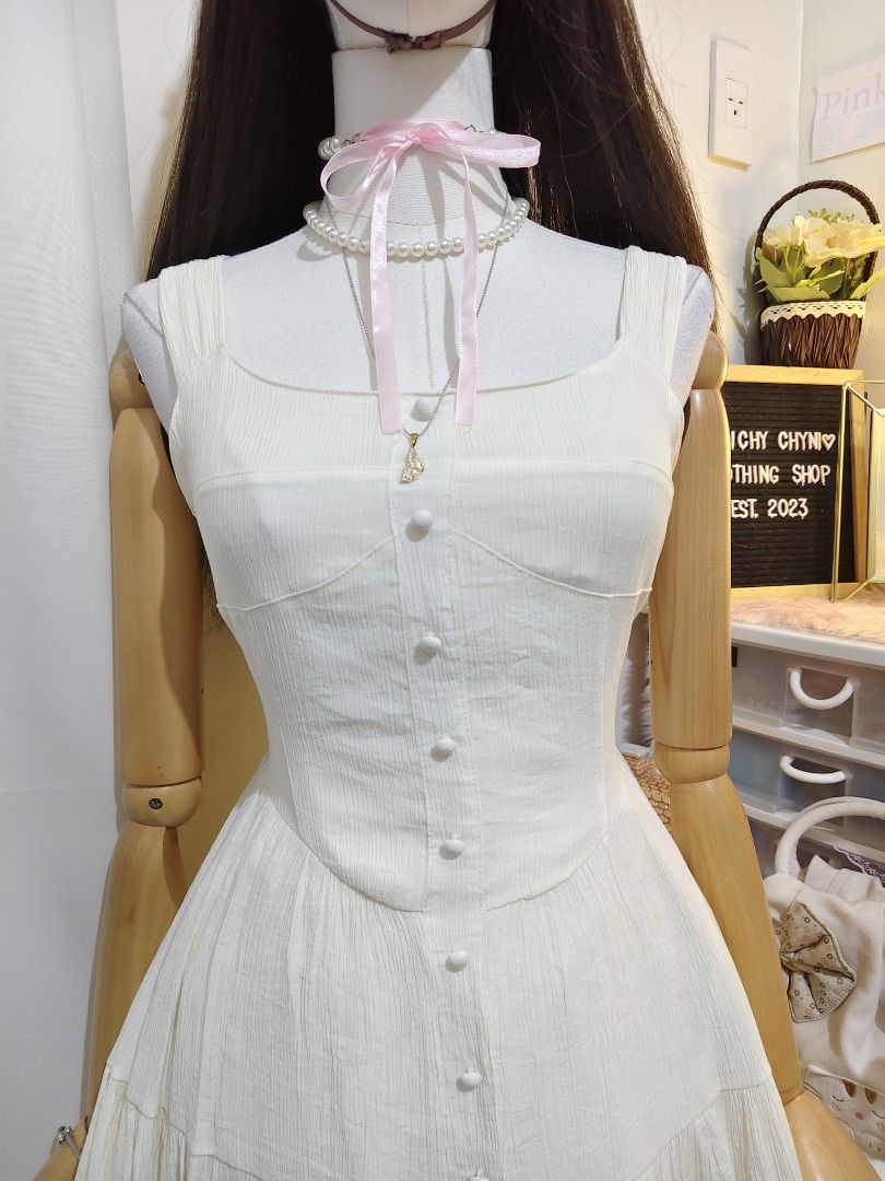 White Corset Style Mini Dress (Category: Dresses) located in Manila. Submitted by chynii_28 (Listing ID 1467624811, Image 2). Description: - Style: White sleeveless mini dress with button-up front detailing - Neckline & Fit: Square neckline and fitted bodice with a flared tiered skirt - Fabric: Lightweight, textured fabric with subtle vertical stripes - Measurements: Bust 32/46", Waist 26/30", Length 32" - Perfect for: Sunny days, casual hangouts