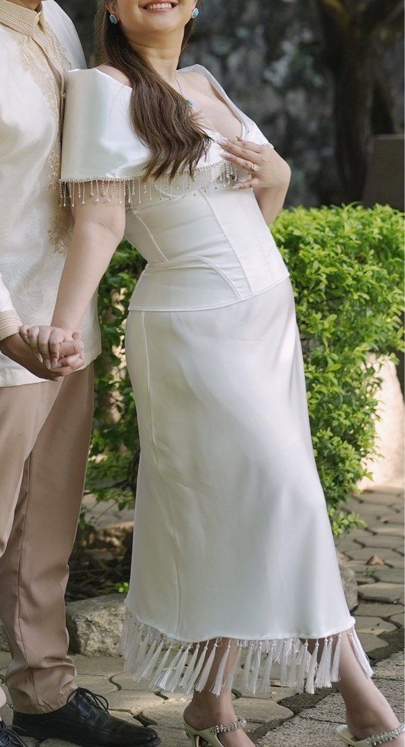 White Satin Pre-wedding Outfit (Category: Evening dresses & gowns) located in Quezon City. Submitted by ericaanderin (Listing ID 1467769595, Image 3). Description: - Color/Material: White satin two-piece set - Style: Structured corset bodice and midi skirt with off-the-shoulder draped sleeves Modern Filipiniana - Details: Delicate fringe tassels along the neckline and hem - Condition: Worn once for a garden photo shoot - Ideal for: Pre-wedding sh