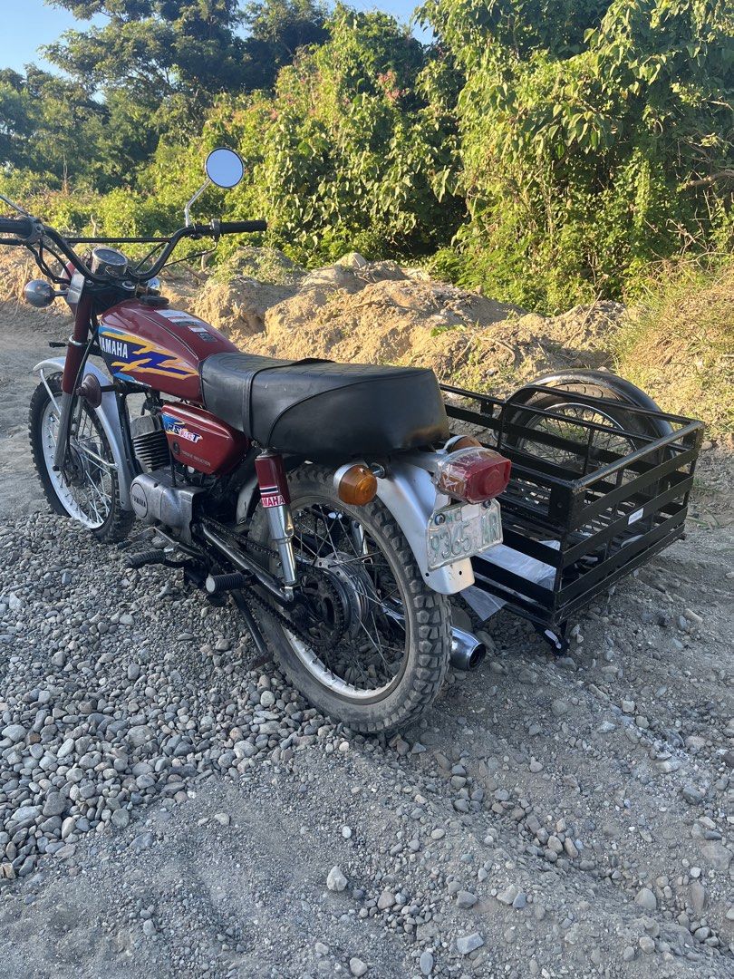 Yamaha RS100 Motorcycle with Sidecar (Category: Motorbikes for Sale) located in Manila. Submitted by rusell_inmotion (Listing ID 1467824764, Image 1). Description: Red Yamaha RS100 motorcycle equipped with a black metal cargo sidecar attached to the right side. Knobby tires installed front and rear. Chrome handlebars fitted with round rearview mirrors. Single bench seat upholstered in black. Chrome front fender and exhaust pipe. Standard round he