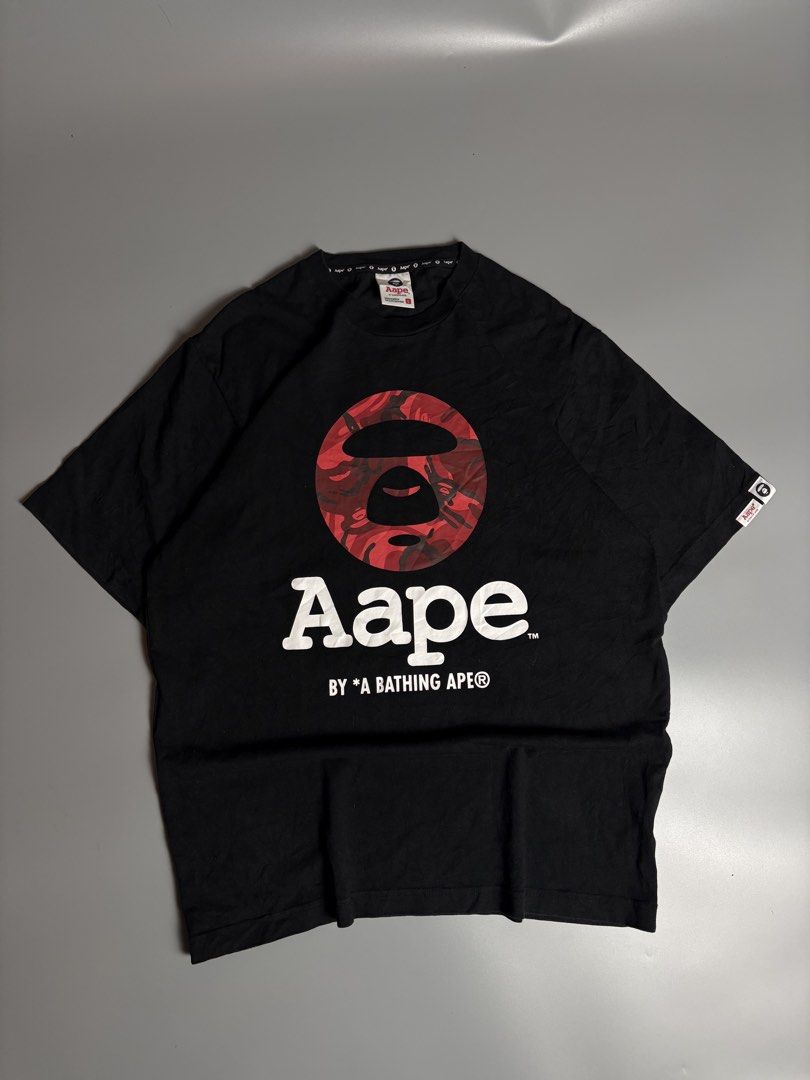 Aape By A Bathing Ape Black Graphic Tee (Category: Tshirts & Polo Shirts ) located in Manila. Submitted by livefalcon-c64e (Listing ID 1467944299, Image 1). Description: - Brand: Aape by A Bathing Ape - Color: Black with bold red camo moon face logo - Size: L (100% cotton) - Details: White text under chest logo, sleeve branding tags, and branded inside neck tape - Condition: Excellent, ready to wear - Perfect for streetwear enthusiasts.