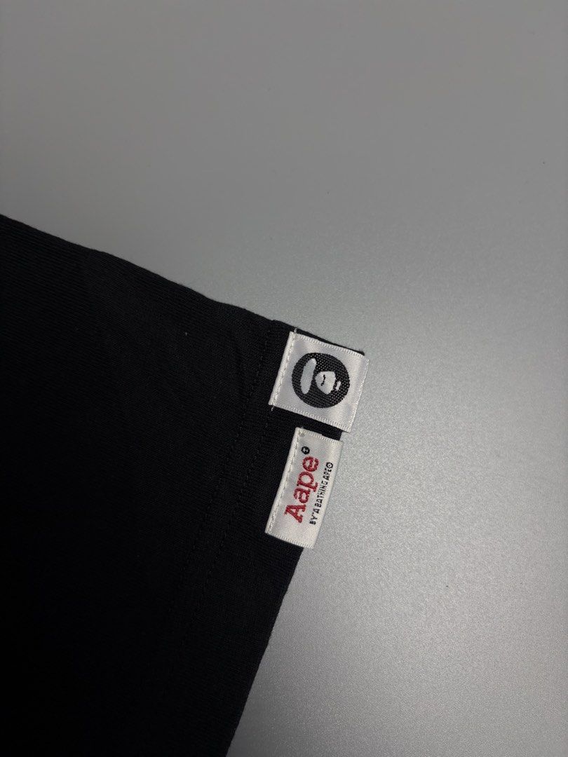 Aape By A Bathing Ape Black Graphic Tee (Category: Tshirts & Polo Shirts ) located in Manila. Submitted by livefalcon-c64e (Listing ID 1467944299, Image 3). Description: - Brand: Aape by A Bathing Ape - Color: Black with bold red camo moon face logo - Size: L (100% cotton) - Details: White text under chest logo, sleeve branding tags, and branded inside neck tape - Condition: Excellent, ready to wear - Perfect for streetwear enthusiasts.