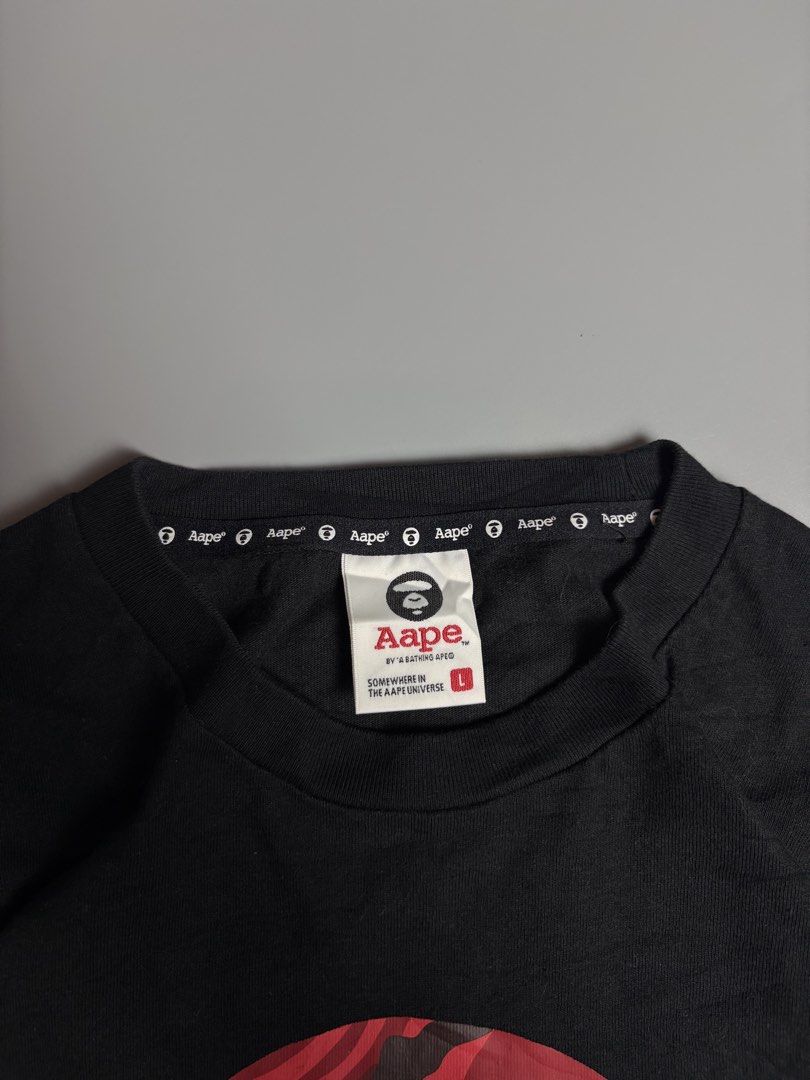 Aape By A Bathing Ape Black Graphic Tee (Category: Tshirts & Polo Shirts ) located in Manila. Submitted by livefalcon-c64e (Listing ID 1467944299, Image 2). Description: - Brand: Aape by A Bathing Ape - Color: Black with bold red camo moon face logo - Size: L (100% cotton) - Details: White text under chest logo, sleeve branding tags, and branded inside neck tape - Condition: Excellent, ready to wear - Perfect for streetwear enthusiasts.