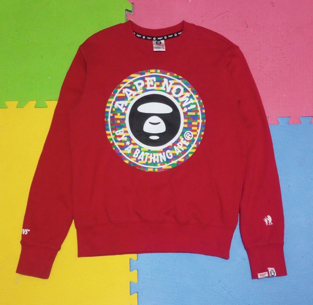 AAPE By A Bathing Ape Red Sweatshirt Size M (Category: Coats, Jackets and Outerwear) located in Las Pinas. Submitted by rzzr_thrift25 (Listing ID 1467939240, Image 1). Description: Red sweatshirt from AAPE by A Bathing Ape. Bold LEGO-style circular logo printed on the chest. Size M tag on the collar. APUNVS text printed on the right sleeve. White embroidered astronaut graphic and branded sleeve tag on the left cuff. Black inner neck tape featurin