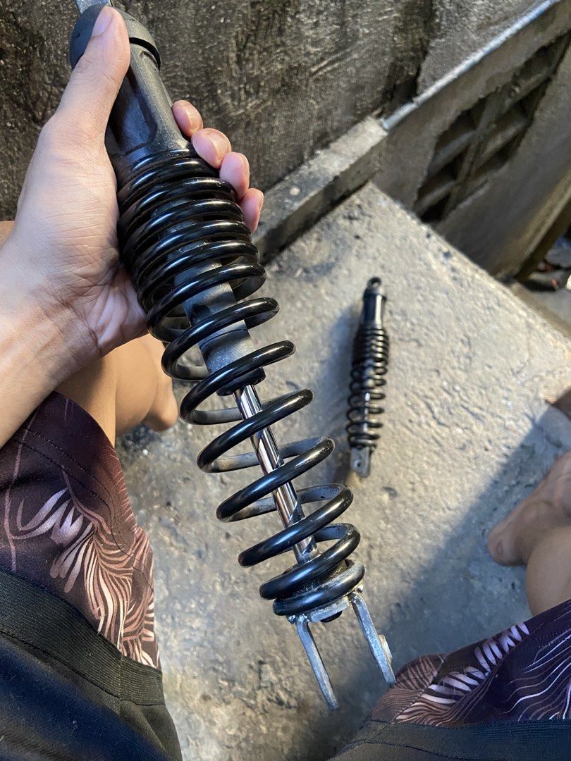 Aerox v2 stock rear shock (Category: Suspension Parts & Accessories) located in Manila. Submitted by almanonjhu33875 (Listing ID 1468007101, Image 2). Description: Pair of motorcycle rear suspension shock absorbers. Black coil springs with metallic lower brackets and upper mounts. Chrome shafts show minor wear. Removed from motorcycle, still in working condition. Standard replacement parts for daily riding. Ready for installation..