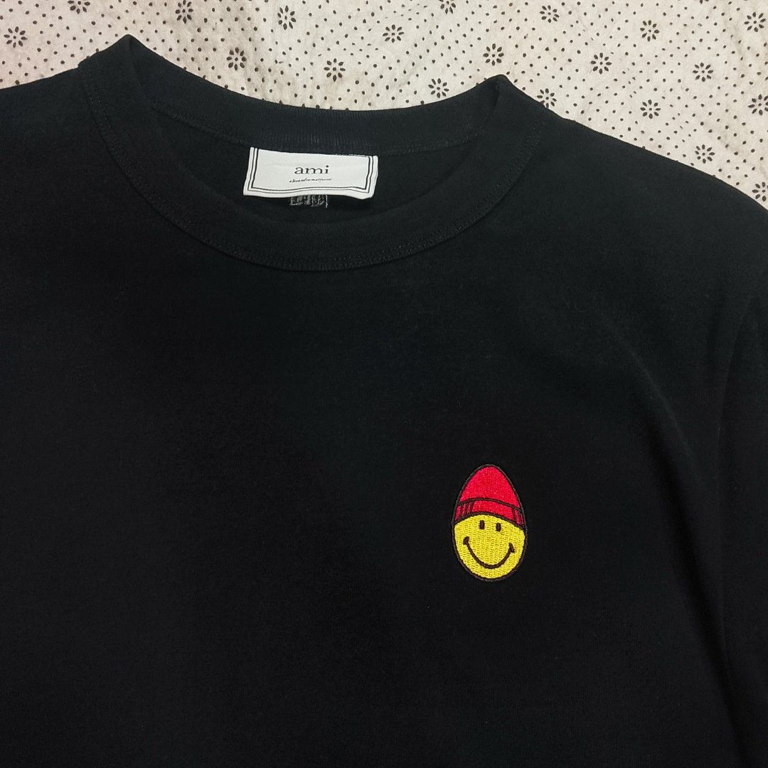 AMI Paris (Alexandre Mattiussi) × Smiley ​ (Category: Tshirts & Polo Shirts ) located in Manila. Submitted by jonahq.9 (Listing ID 1467936788, Image 1). Description: - Brand: AMI Paris (Alexandre Mattiussi) × Smiley ​19x25 dimes - Style: Short-sleeve crew neck tee ​ - Color: Black ​ - Design: Embroidered Smiley face with red AMI heart/beanie on left chest ​ - Fabric: Soft premium cotton ​ - Origin: Made in Portugal (with love) — matches official 