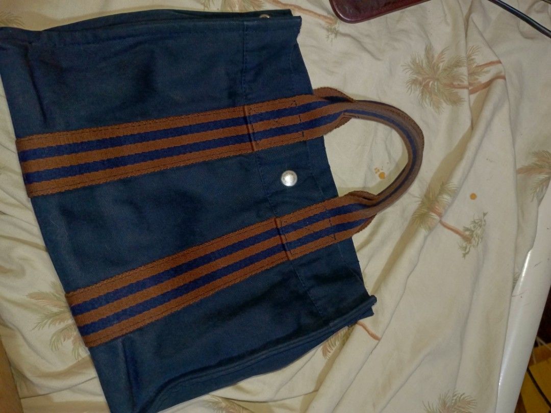 AUTHENTIC Hermes Herbag Canvas Tote Bag (Category: Luxury Bags & Wallets) located in Pililla. Submitted by stephenivan (Listing ID 1468055210, Image 2). Description: Navy blue canvas tote bag with brown and navy striped web handles. Silver-tone hardware snap button on the front stamped with Hermes. Interior features zippered pocket with branded zipper pull and fabric logo tag reading Hermes Paris. Durable canvas material. Great everyday size for 