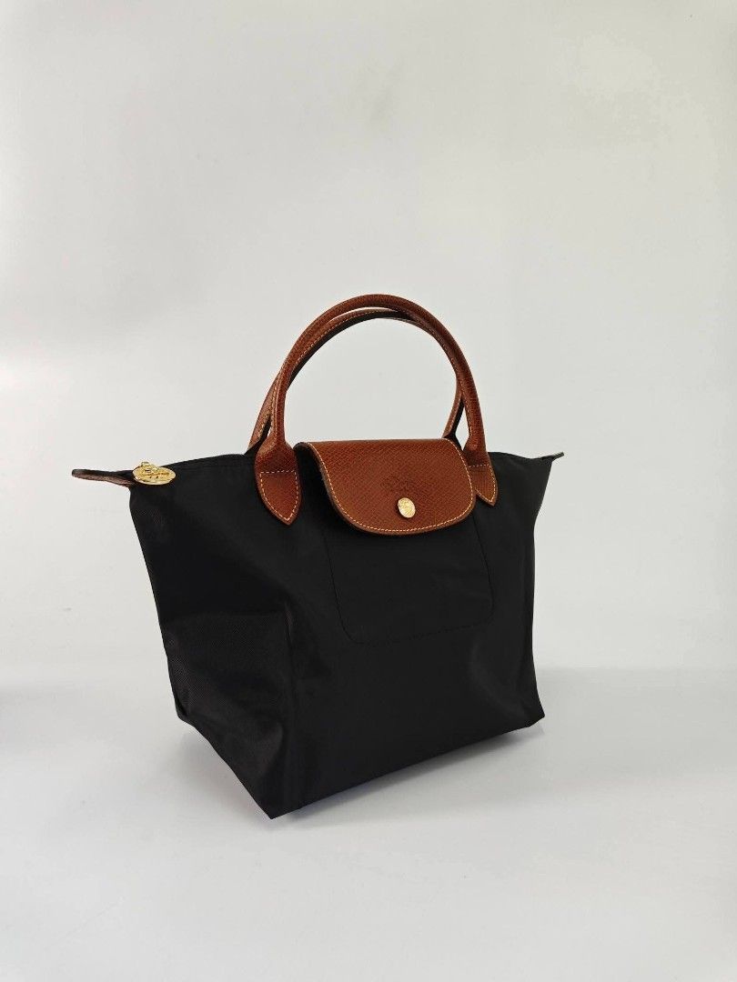 Authentic Longchamp Classic Le Pliage Small Short Handle Nylon Hand Bag - Black (Category: Purses & Pouches) located in Quezon City. Submitted by hollowwillow (Listing ID 1468014605, Image 2). Description: - Color: Black nylon with brown leather handle and flap - Closure: Top zip with gold-tone hardware and snap button on front flap - Interior: Roomy with a small slip pocket - Design: Foldable, lightweight, and structured .