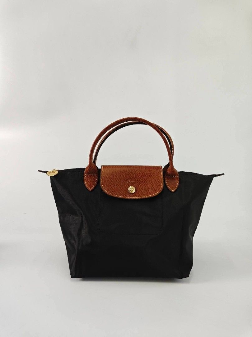 Authentic Longchamp Classic Le Pliage Small Short Handle Nylon Hand Bag - Black (Category: Purses & Pouches) located in Quezon City. Submitted by hollowwillow (Listing ID 1468014605, Image 1). Description: - Color: Black nylon with brown leather handle and flap - Closure: Top zip with gold-tone hardware and snap button on front flap - Interior: Roomy with a small slip pocket - Design: Foldable, lightweight, and structured .