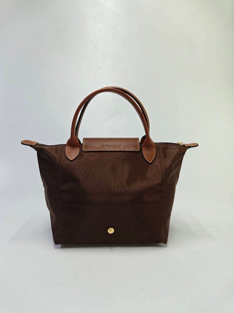 Authentic Longchamp Le Pliage Small Short Handle Tote Bag - Ebony (Category: Tote Bags) located in Quezon City. Submitted by hollowwillow (Listing ID 1467858691, Image 3). Description: - Color: Brown - Material: Durable nylon with brown leather top handles and flap - Hardware: Gold-tone with jockey medallion zipper pull - Storage: Main compartment with internal slip pocket - Feature: Foldable design for easy storage - Style: Classic and versatile