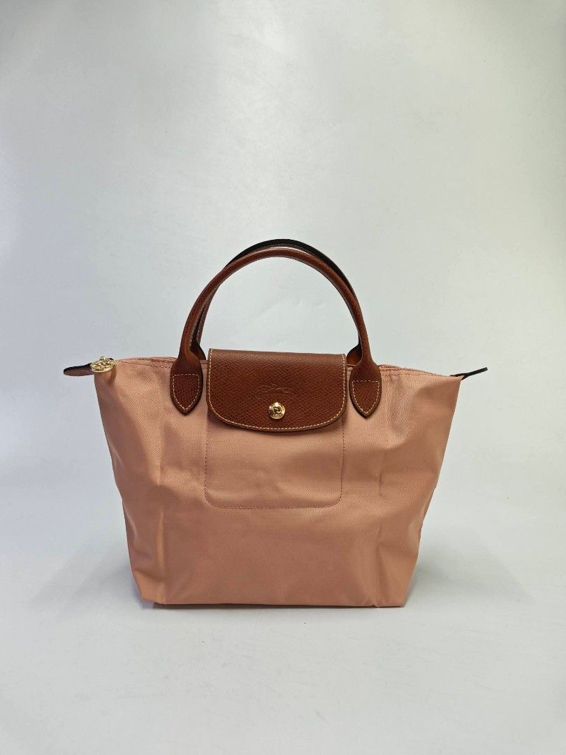Authentic Longchamp Le Pliage Small Short Handle Top Handle Bag - Pink Tea (Category: Tote Bags) located in Quezon City. Submitted by hollowwillow (Listing ID 1467859083, Image 1). Description: - Authentic Longchamp Le Pliage Top Handle Bag - Color: Charming pink nylon with signature brown leather flap and handles - Hardware: Gold-tone snap closure and zipper - Interior: Clean lining with convenient slip pockets - Features: Iconic foldable design