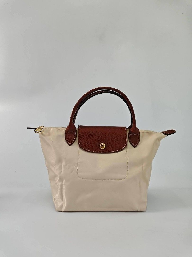 Authentic Longchamp Le Pliage Classic Small Short Handle Handbag - Papier (Category: Purses & Pouches) located in Quezon City. Submitted by hollowwillow (Listing ID 1467991256, Image 1). Description: - Color: papier - Hardware: Polished gold-tone hardware with a secure zipper closure - Interior: Clean cream lining equipped with handy open slip pockets - Design: Structured bottom for stability and a classic top handle style .