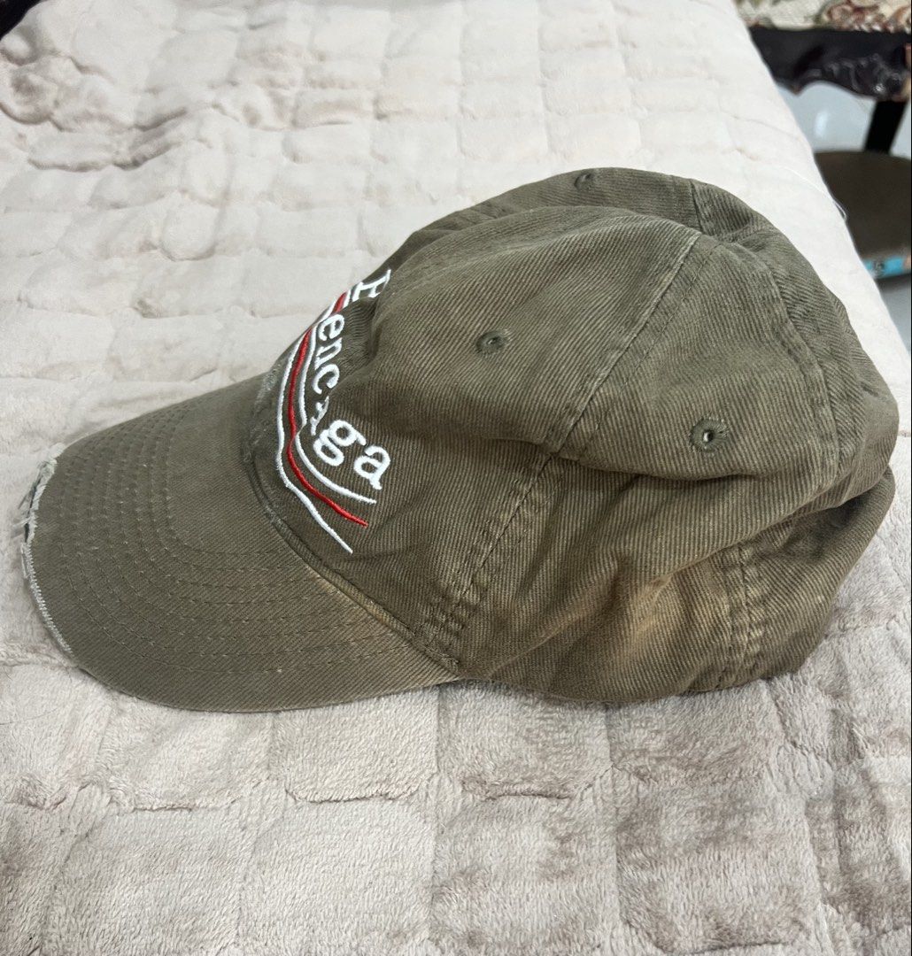 Balenciaga Political Campaign Distressed Baseball Cap (Category: Caps & Hats) located in Imus. Submitted by eacaps (Listing ID 1467895607, Image 2). Description: A khaki/olive green baseball cap featuring embroidered Balenciaga lettering with red and white stripe detailing across the front. Details: Brand: Balenciaga Color: Khaki / Olive Green Embroidered front logo Curved brim Adjustable back strap Made in Portuga Condition: Pre-owned. The cap f