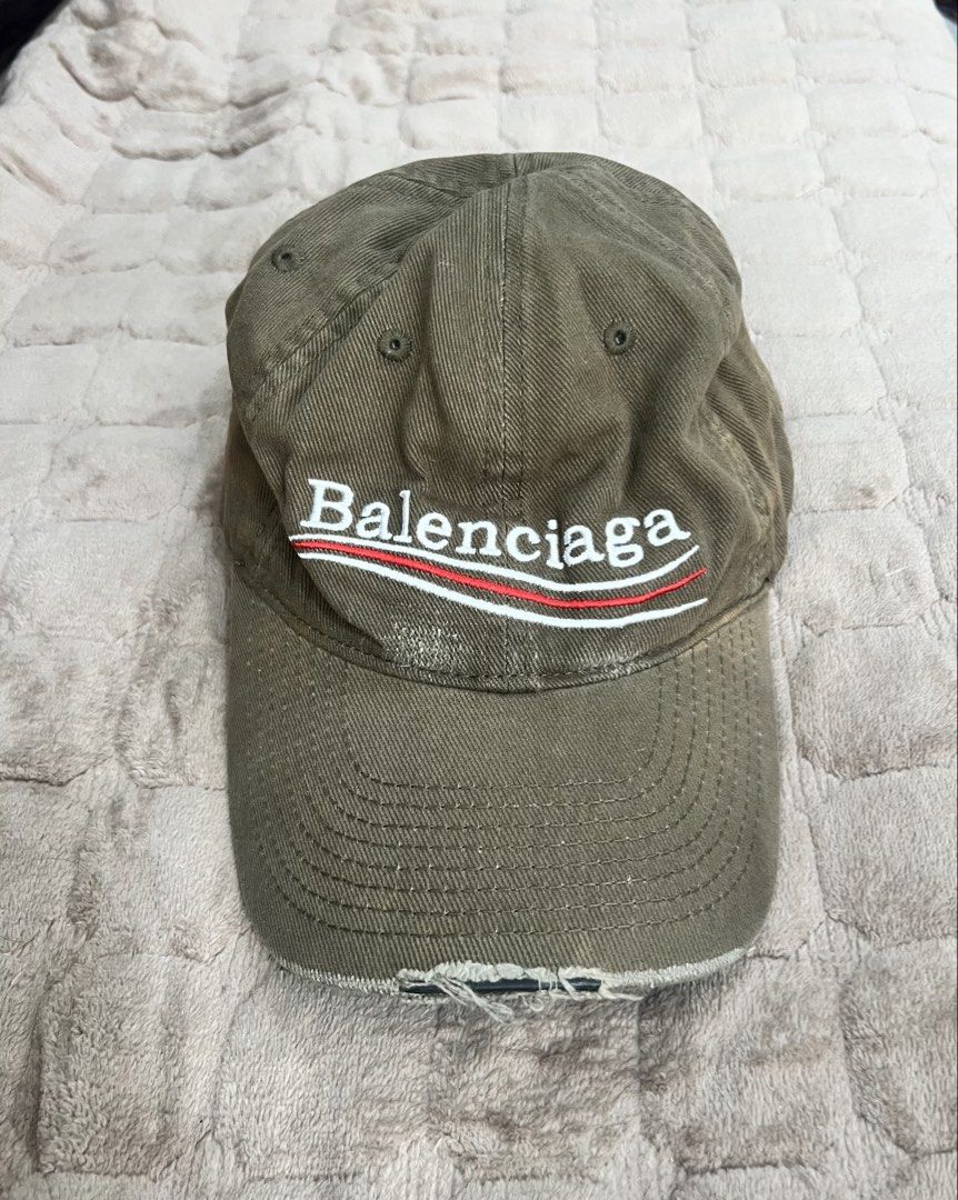 Balenciaga Political Campaign Distressed Baseball Cap (Category: Caps & Hats) located in Imus. Submitted by eacaps (Listing ID 1467895607, Image 1). Description: A khaki/olive green baseball cap featuring embroidered Balenciaga lettering with red and white stripe detailing across the front. Details: Brand: Balenciaga Color: Khaki / Olive Green Embroidered front logo Curved brim Adjustable back strap Made in Portuga Condition: Pre-owned. The cap f