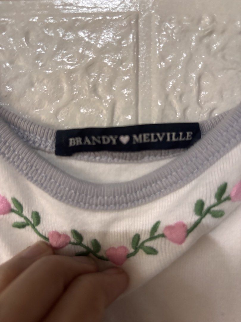 Brandy Melville cami top (Category: Sleeveless) located in Cebu City. Submitted by airahxoxo (Listing ID 1467916497, Image 2). Description: - Brand: Brandy Melville - Style: White camisole tank top with lettuce hem - Details: Grey trim on neckline and straps - Design: Pink heart and green vine embroidery on the chest - Condition: Excellent / Great find! - Mode of Payment: Gcash / BPI - Shipping: Via J&T Express (MMP/Provincial).