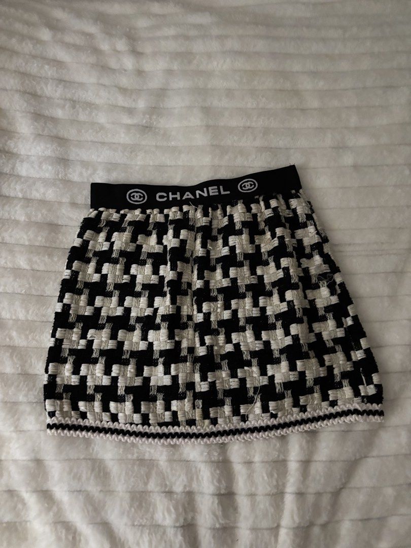 Chanel Black White Houndstooth Tweed Mini Skirt (Category: Skirts) located in Quezon City. Submitted by hadescloset (Listing ID 1468029524, Image 2). Description: - Style: Black and white houndstooth tweed mini skirt - Waistband: Elastic with bold white Chanel lettering and logo branding - Fit: Structured flared cut - Details: Scalloped trim finish along the bottom hem - Styling: Pairs easily with basic black tops and tees.