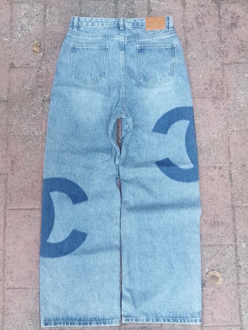 Chanel Denim Jeans with Logo Print (Category: Jeans) located in Munoz. Submitted by rogelioarq16817 (Listing ID 1467975038, Image 2). Description: - Light wash denim jeans with statement CC logo print down the legs - Classic straight leg cut with a comfortable mid-rise fit - Standard button closure, belt loops, and classic 5-pocket styling - Features a stylish brown leather patch on the back waistband - Versatile and perfect for casual everyday w