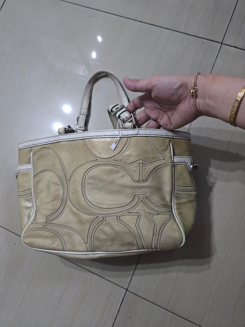 Coach Tote/ Shoulderbag (Category: Luxury Bags & Wallets) located in Manila. Submitted by brandedshoppe_mnl (Listing ID 1467987685, Image 1). Description: - Brand: Coach - Material: Metallic gold leather with white leather trim - Hardware: Silver-tone with protective metal feet on the base - Closure & Straps: Turn-lock side closure with dual buckled shoulder straps - Design: Signature embossed pattern on front and back - Inclusion: Includes match