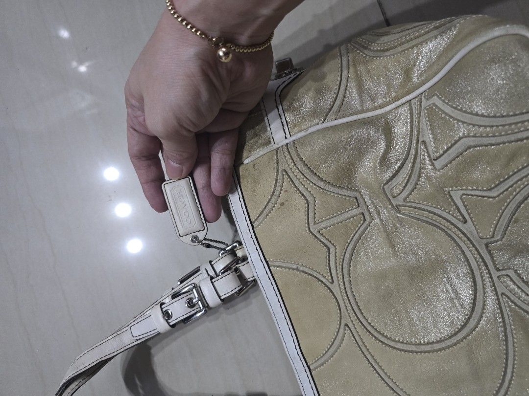 Coach Tote/ Shoulderbag (Category: Luxury Bags & Wallets) located in Manila. Submitted by brandedshoppe_mnl (Listing ID 1467987685, Image 3). Description: - Brand: Coach - Material: Metallic gold leather with white leather trim - Hardware: Silver-tone with protective metal feet on the base - Closure & Straps: Turn-lock side closure with dual buckled shoulder straps - Design: Signature embossed pattern on front and back - Inclusion: Includes match