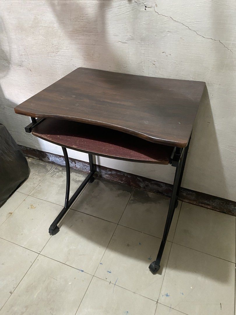 Compact Computer Desk with Keyboard Tray and Wheels (Category: Office Furniture & Fixtures) located in Imus. Submitted by nhelsg2 (Listing ID 1467899877, Image 3). Description: Compact computer desk with a pull-out keyboard tray. Dark wood-grain top with a curved front edge. Black metal frame with curved legs on rolling caster wheels. Lower keyboard shelf shows noticeable surface wear and scuffing from past use. Handy rolling workstation for a sm