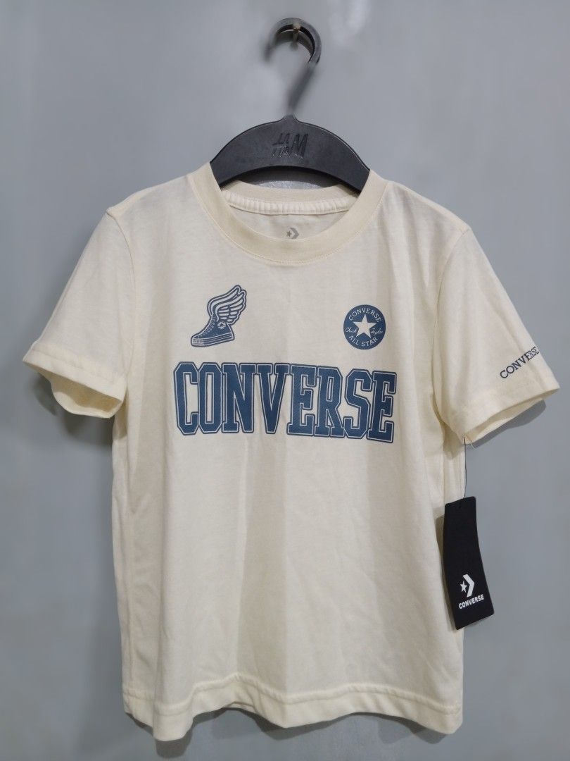 Converse T-shirt for 4-6 Boys (Category: Babies & Kids Fashion) located in Bacoor. Submitted by thriftworksph (Listing ID 1467936133, Image 1). Description: - Brand: Converse - Color: Cream - Size: Large - Condition: Brand new with original black tag attached - Design: Blue block lettering with winged Chuck Taylor graphic and star logo on the chest - Details: Short sleeves with small Converse branding on the left sleeve 18" length 15" bust.