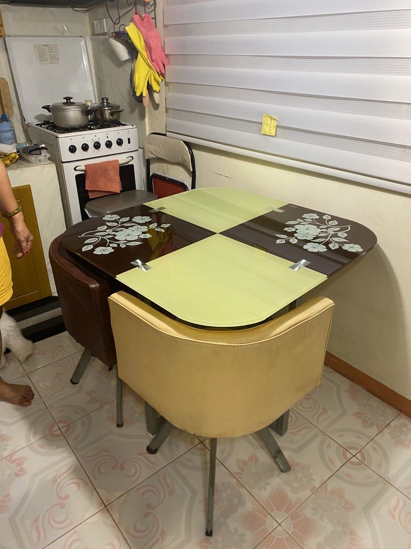 Dining table set with 4 swivel chairs (Category: Tables & Sets) located in Imus. Submitted by nhelsg2 (Listing ID 1467870605, Image 1). Description: - Dining set includes 1 square glass table and 4 matching armchairs - Table features a unique design with two green and two dark brown panels with floral prints - 4 armchairs: 2 in beige and 2 in dark brown - Chairs come with metal legs and a smooth 360-degree swivel function - ideal for compact kitc