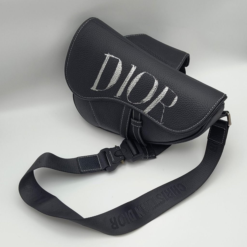 Dior x Alex Foxton Saddle Bag Black (Category: Luxury Bags & Wallets) located in Lapu Lapu. Submitted by theluxxaffair (Listing ID 1468050695, Image 2). Description: Dior Men x Alex Foxton Saddle bag crafted in black grained calfskin leather with contrasting white stitching and oversized DIOR lettering across the flap. Features the signature curved Saddle silhouette, adjustable Christian Dior nylon shoulder strap with industrial-style CD buckle, 