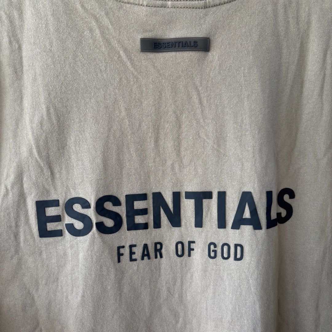 Essential tee shirt (Category: Tshirts & Polo Shirts ) located in San Fernando. Submitted by diff.thr1ft (Listing ID 1467865086, Image 3). Description: - Brand: ESSENTIALS Fear of God - Color: Brown / Earth tone - Size: Medium (M) - Material: 100% cotton, made in Vietnam - Condition: 4/4, well-maintained - Features bold ESSENTIALS Fear of God back lettering and rubberized collar logo patch.