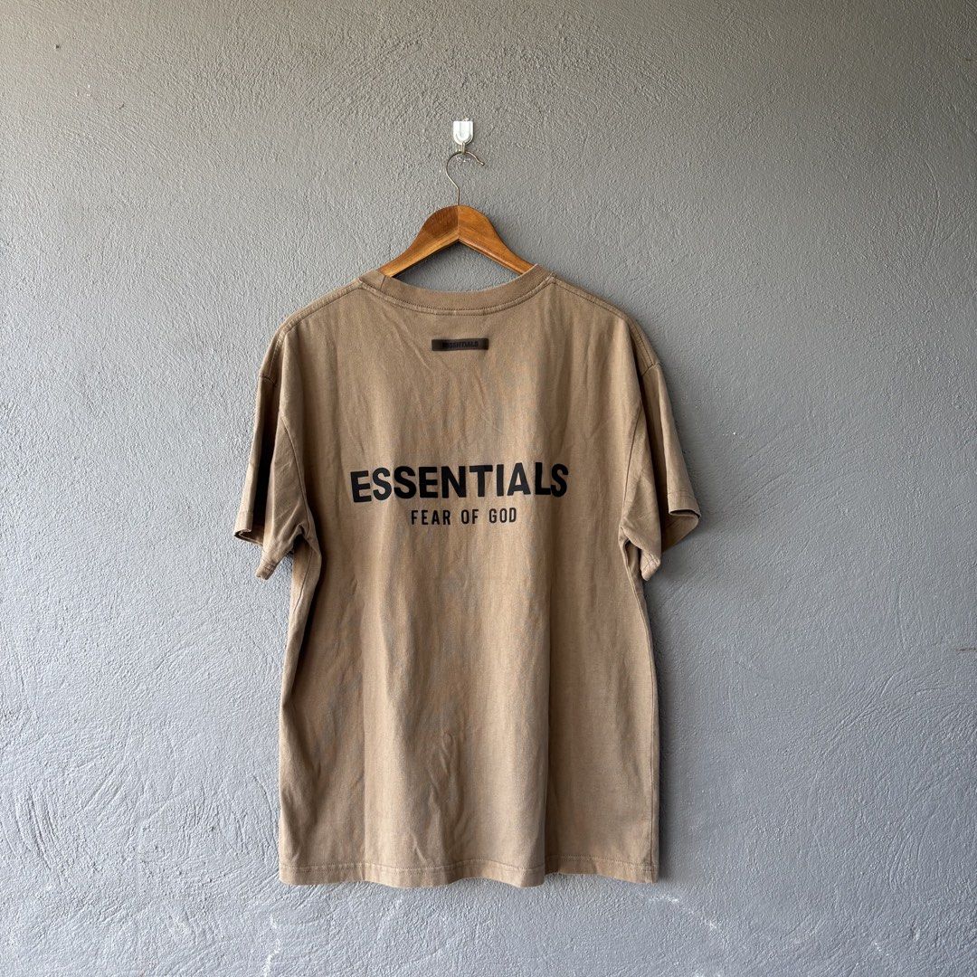 Essential tee shirt (Category: Tshirts & Polo Shirts ) located in San Fernando. Submitted by diff.thr1ft (Listing ID 1467865086, Image 1). Description: - Brand: ESSENTIALS Fear of God - Color: Brown / Earth tone - Size: Medium (M) - Material: 100% cotton, made in Vietnam - Condition: 4/4, well-maintained - Features bold ESSENTIALS Fear of God back lettering and rubberized collar logo patch.