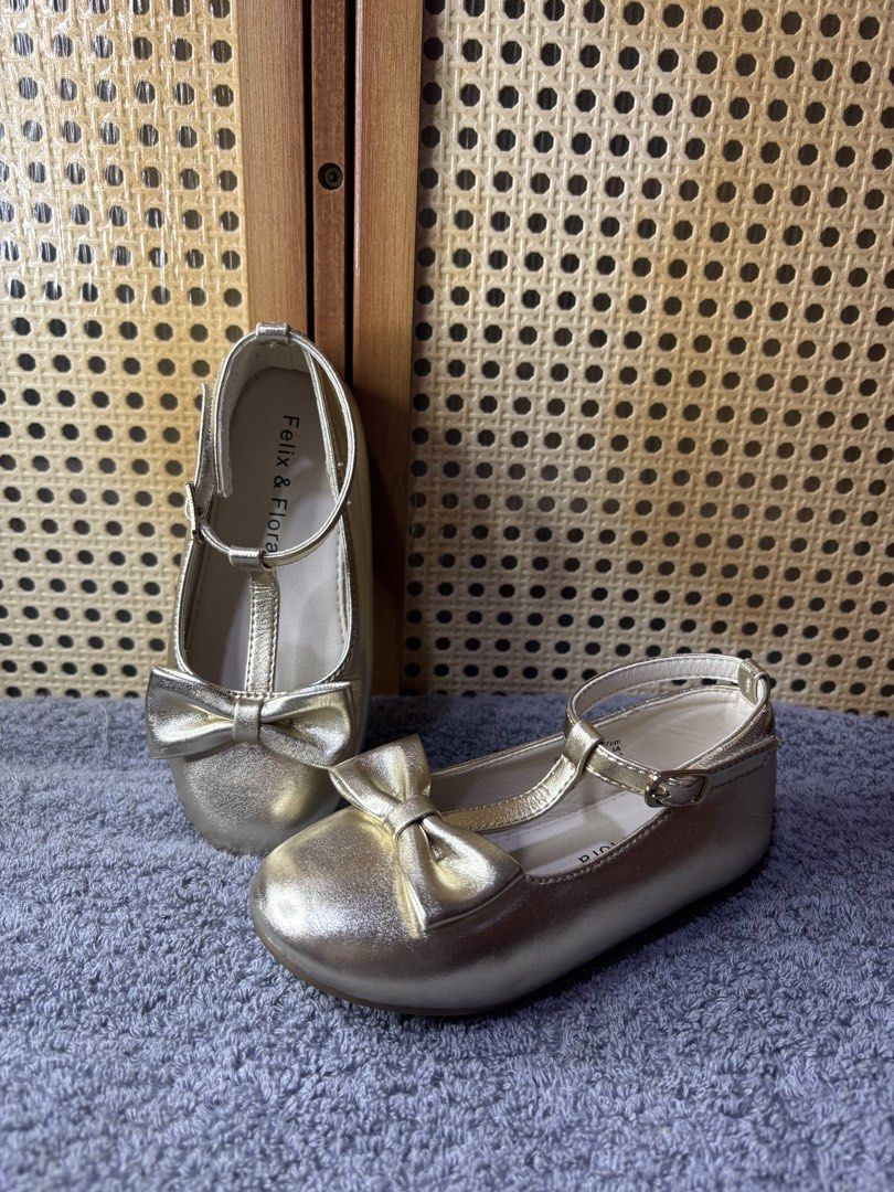 Felix & Flora Gold T-Bar Flats with Bow (Category: Babies & Kids Fashion) located in Manila. Submitted by wardrobeinmnl (Listing ID 1467892049, Image 1). Description: Size: 10 - Brand: Felix & Flora - Color/Finish: Gold metallic - Design: T-bar strap with buckle closure and cute toe bow - Condition: Clean insoles and neat stitching - Versatile: Great for parties, weddings, or everyday wear.