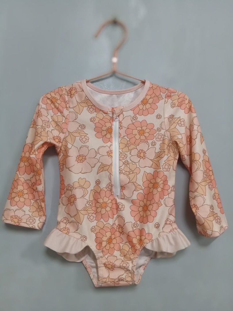 Floral Long Sleeve Swimsuit Size 110 (Category: Babies & Kids Fashion) located in Bacoor. Submitted by thriftworksph (Listing ID 1467938021, Image 1). Description: - Brand: Miledii - Item: Kids long sleeve swimsuit - Design: Cream base with all-over orange and peach floral pattern - Features: Half-zip front with white zipper, adorable ruffle detail around leg openings - Size: 110 (Tag) - Material: 65% polyester, 35% elastane - Manufacture Date: O