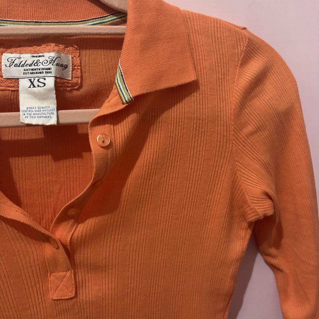 Folded & Hung Orange Ribbed Polo Top Size XS (Category: Shirts) located in Taguig. Submitted by xoalexv (Listing ID 1468010363, Image 3). Description: - Brand: Folded & Hung - Size: XS - Color: Bright orange - Material: Soft, stretchy ribbed knit fabric - Design: Collared neckline, button placket, 3/4 sleeves - Fit: Fitted cut - Perfect for layering or everyday casual wear.