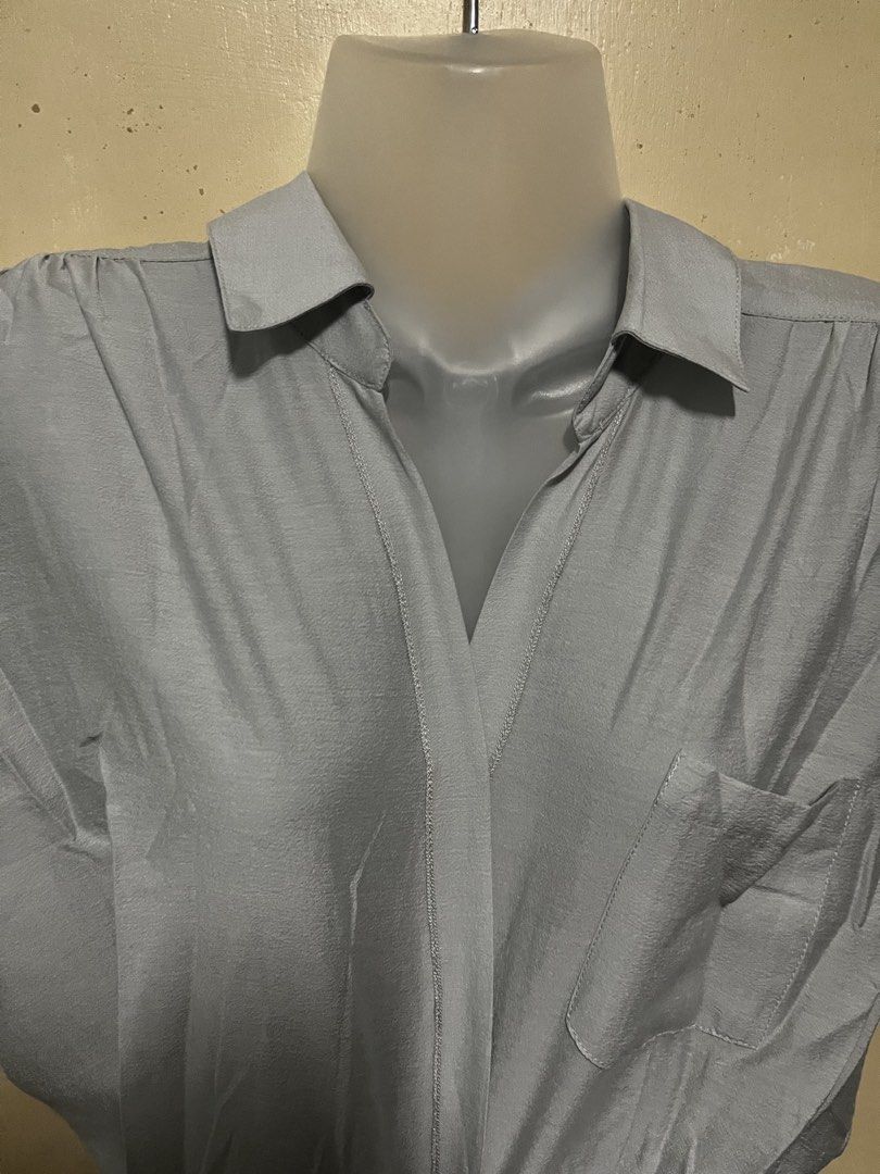 Grey Collared Short Sleeve Blouse with Pocket (Category: Blouses) located in Tabuk. Submitted by zenwolf-1867 (Listing ID 1467973584, Image 2). Description: - Color: Light grey - Style: Short-sleeve button-down blouse with pointed collar - Fit: Relaxed fit with a slight drape - Details: Single chest pocket on the right side - Material: Smooth, lightweight, and comfortable - Versatility: Ideal for casual days or office wear, pairs easily with jean