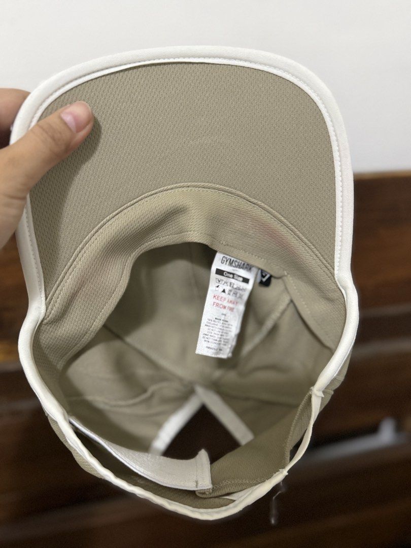 Gymshark Beige Running Cap (Category: Activewear) located in Caloocan City. Submitted by bellita_05 (Listing ID 1468023714, Image 3). Description: - Brand: Gymshark - Color: Khaki beige with white trim along the brim - Features: Ponytail hole cut out for workouts, super lightweight mesh fabric - Branding: Gymshark logo printed on the front - Fit: One size fits all with an adjustable strap - Condition: Inner wash tag intact.