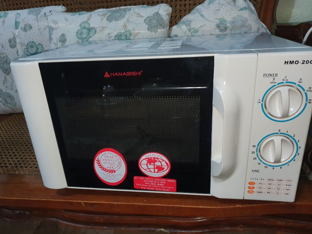 Hanabishi MICROWAVE Oven HMO-20G 20L (Category: Ovens & Toasters) located in Quezon City. Submitted by carbonfootprint (Listing ID 1467946804, Image 3). Description: ✔️Hanabishi microwave oven model ✔️HMO-20G with twenty-liter capacity. ✔️Includes original box, rotating glass plate, and interior roller ring. ✔️Dual rotary dials control power levels and cooking timer. ✔️White exterior housing with black front door panel and red branding. NEVER USE