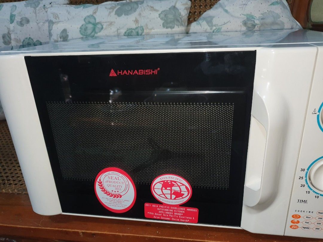 Hanabishi MICROWAVE Oven HMO-20G 20L (Category: Ovens & Toasters) located in Quezon City. Submitted by carbonfootprint (Listing ID 1467946804, Image 2). Description: ✔️Hanabishi microwave oven model ✔️HMO-20G with twenty-liter capacity. ✔️Includes original box, rotating glass plate, and interior roller ring. ✔️Dual rotary dials control power levels and cooking timer. ✔️White exterior housing with black front door panel and red branding. NEVER USE
