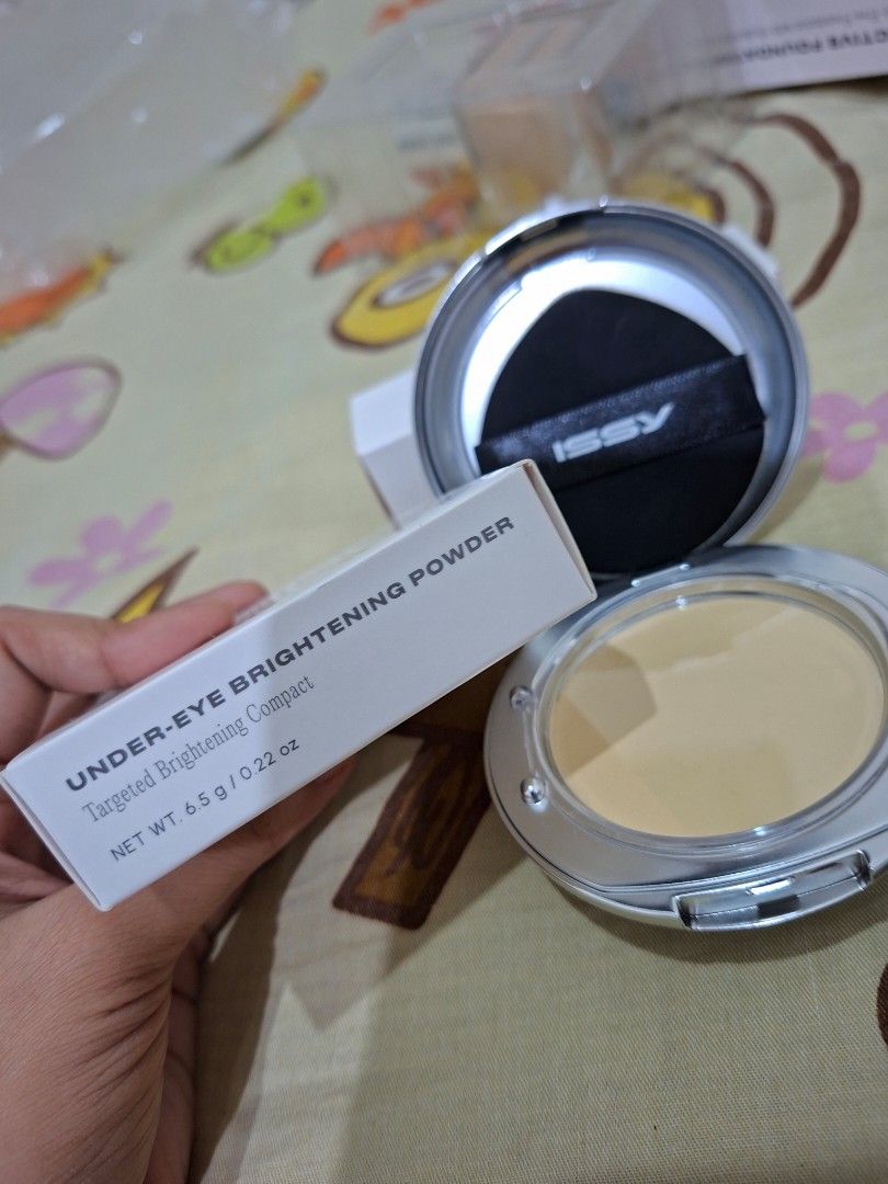 Issy Under-Eye Brightening Powder Compact (Category: Makeup) located in Manila. Submitted by anachibi (Listing ID 1467871458, Image 2). Description: - Brand: Issy - Item: Under-eye brightening powder compact - Shade: Pale yellow - Condition: Used for swatching only - RFS: Wrong Shade - Inclusions: Original white box, round silver compact case, and black puff applicator with Issy logo strap.