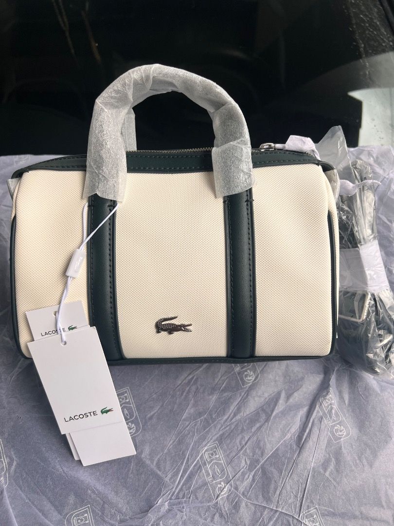 Lacoste Canvas Mini Barrel Handbag (Category: Luxury Bags & Wallets) located in Mandaluyong City. Submitted by happystone-8b18 (Listing ID 1468055673, Image 2). Description: - Brand: Lacoste - Style: Mini barrel bag - Color: Off-white canvas with dark green leather trim - Hardware/Details: Metal crocodile logo on front, top zipper closure, double top handles - Strap: Includes detachable shoulder strap (still wrapped in original plastic) - Conditi