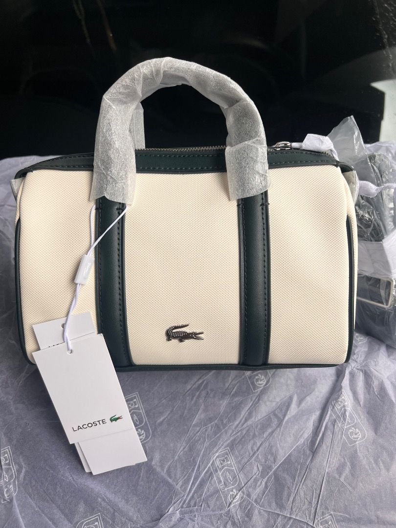 Lacoste Canvas Mini Barrel Handbag (Category: Luxury Bags & Wallets) located in Mandaluyong City. Submitted by happystone-8b18 (Listing ID 1468055673, Image 1). Description: - Brand: Lacoste - Style: Mini barrel bag - Color: Off-white canvas with dark green leather trim - Hardware/Details: Metal crocodile logo on front, top zipper closure, double top handles - Strap: Includes detachable shoulder strap (still wrapped in original plastic) - Conditi