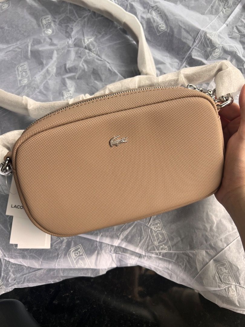 Lacoste Crossbody Bag Beige (Category: Cross-body Bags) located in Mandaluyong City. Submitted by happystone-8b18 (Listing ID 1468055587, Image 2). Description: - Brand: Lacoste - Style: Camera bag / Crossbody - Color: Taupe (textured material) - Hardware: Silver-tone with metallic crocodile logo - Closure: Top zipper - Strap: Adjustable and detachable with matching clips - Condition: Brand new with original tags and protective wrapping intact.