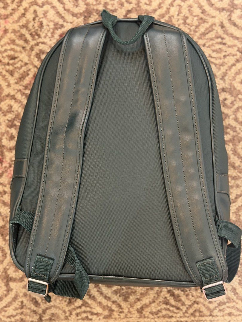 Lacoste Green Backpack with Front Pocket (Category: Backpacks) located in Taguig. Submitted by markitopinas (Listing ID 1467869244, Image 2). Description: Dark green Lacoste backpack with white branding on the front pocket. Textured synthetic material with smooth panels. Padded shoulder straps with adjustable buckles. Extra front zip compartment and top grab handle. Velcro closure inside the front slip pocket. Clean dark interior lining. Solid ev