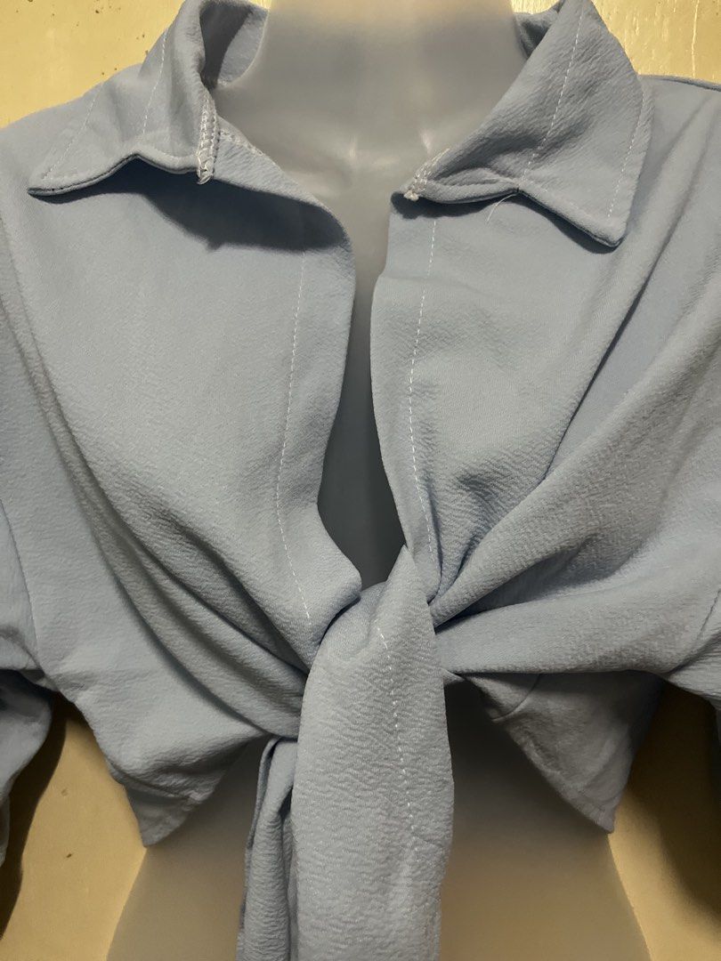 Light Blue Cropped Tie-Front Shirt Blouse (Category: Blouses) located in Tabuk. Submitted by zenwolf-1867 (Listing ID 1467973459, Image 2). Description: - Color: Light blue - Style: Collared crop top with half sleeves and front-tie knot - Fabric: Textured, lightweight, and breathable - Versatility: Pairs easily with high-waisted jeans, shorts, or skirts - Condition: Brand new / Excellent (ready to wear).