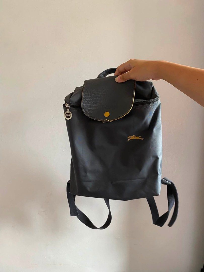 Longchamp Le Pliage Nylon Backpack Grey (Category: Backpacks) located in Iloilo. Submitted by clariceanyanicole (Listing ID 1467925439, Image 1). Description: - Material: Durable grey nylon with dark leather flap and gold snap button closure - Branding: Iconic gold horse logo embroidered on the front pocket - Hardware: Gold zipper pull with smooth zip opening - Comfort: Adjustable black fabric shoulder straps and top handle - Condition: Clean sti