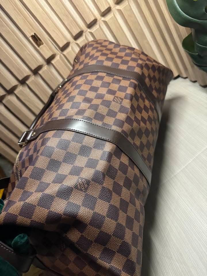 Louis Vuitton Damier Ebene Keepall Bandouliere (Category: Luxury Bags & Wallets) located in Manila. Submitted by goodbuying_items0211 (Listing ID 1467969207, Image 2). Description: - Louis Vuitton travel duffel in classic Damier Ebene canvas - Dark brown leather trim and polished gold-tone hardware - Spacious red fabric interior featuring a convenient zip pocket - Includes matching shoulder strap, padlock, and keys - Clean condition inside and ou