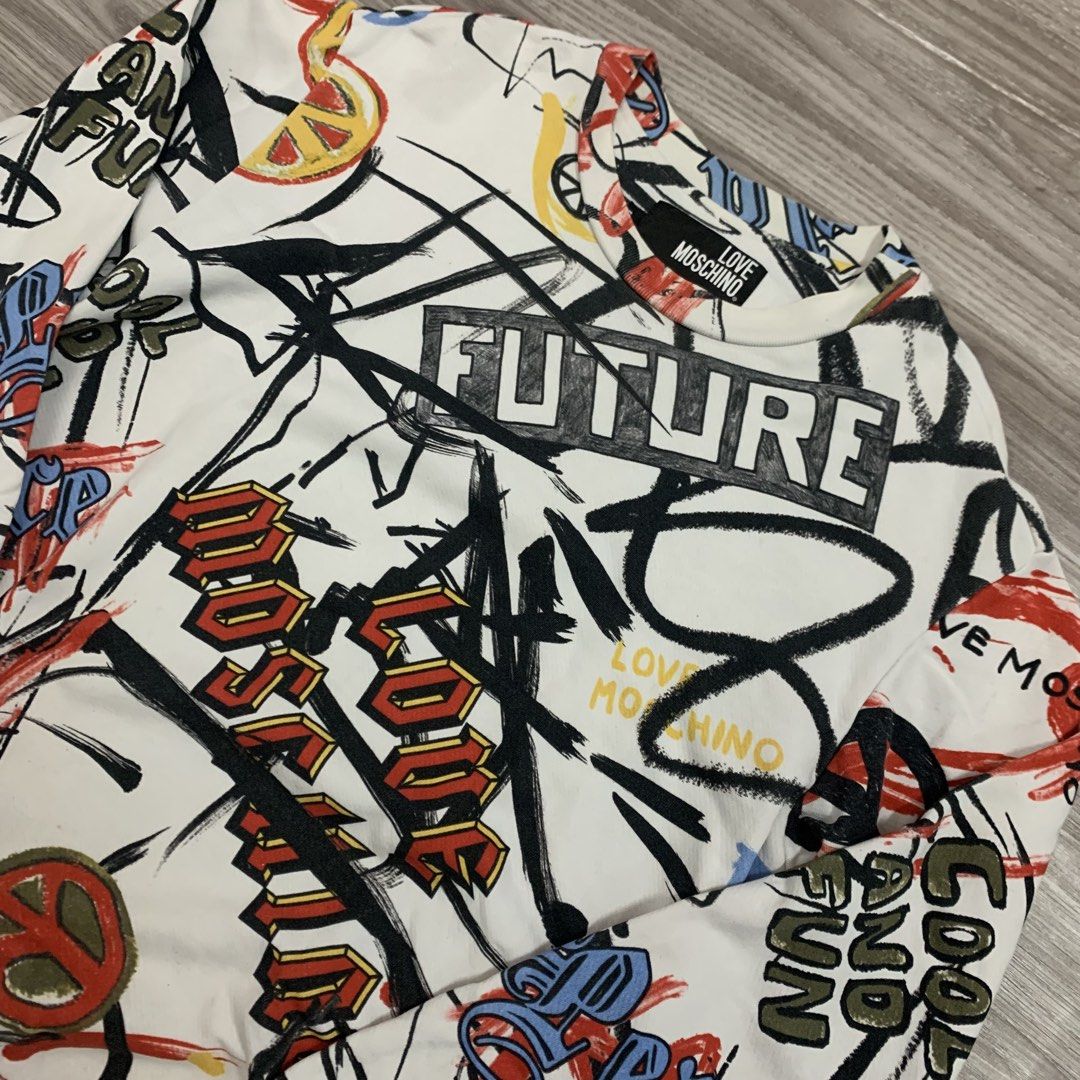 Love Moschino Graffiti Print Sweatshirt (Category: Longsleeves) located in Cavite. Submitted by yobubsss (Listing ID 1468050283, Image 2). Description: - Brand: Love Moschino - Color: White with vibrant all-over graffiti print (FUTURE, LOVE MOSCHINO, peace signs) - Size: Small (neck tag attached) - Material: Soft cotton blend - Details: Long sleeves, ribbed cuffs and hem, inner care label included - Condition: Brand new with tags.