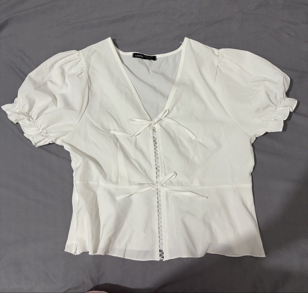 Lovito White Puff Sleeve Bow Tie Front Blouse (Category: Blouses) located in Taguig. Submitted by katalonia (Listing ID 1467978649, Image 1). Description: - Brand: Lovito - Color: White - Style: Peplum blouse with V-neck and front bow ties - Details: Short puff sleeves, ruffled cuffs, and decorative ladder stitching - Fabric: Lightweight and comfortable - Perfect for: Casual outings, dates, or everyday wear - Condition: Brand new / Excellent - 41