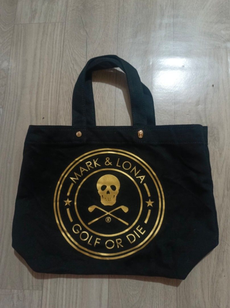 Mark & Lona Black Canvas Golf Tote Bag (Category: Tote Bags) located in Digos. Submitted by jenepiisid83759 (Listing ID 1467986880, Image 1). Description: - Brand: Mark & Lona - Color: Black canvas with gold metallic hardware - Design: Front graphic print with skull, golf clubs, and 'Golf Or Die' text - Details: Gold-toned metallic studs and signature skull-shaped stud near the top edge - Straps: Twin black fabric handles for comfortable carrying