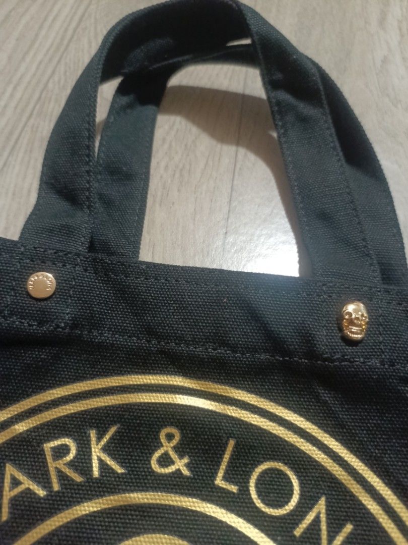Mark & Lona Black Canvas Golf Tote Bag (Category: Tote Bags) located in Digos. Submitted by jenepiisid83759 (Listing ID 1467986880, Image 3). Description: - Brand: Mark & Lona - Color: Black canvas with gold metallic hardware - Design: Front graphic print with skull, golf clubs, and 'Golf Or Die' text - Details: Gold-toned metallic studs and signature skull-shaped stud near the top edge - Straps: Twin black fabric handles for comfortable carrying