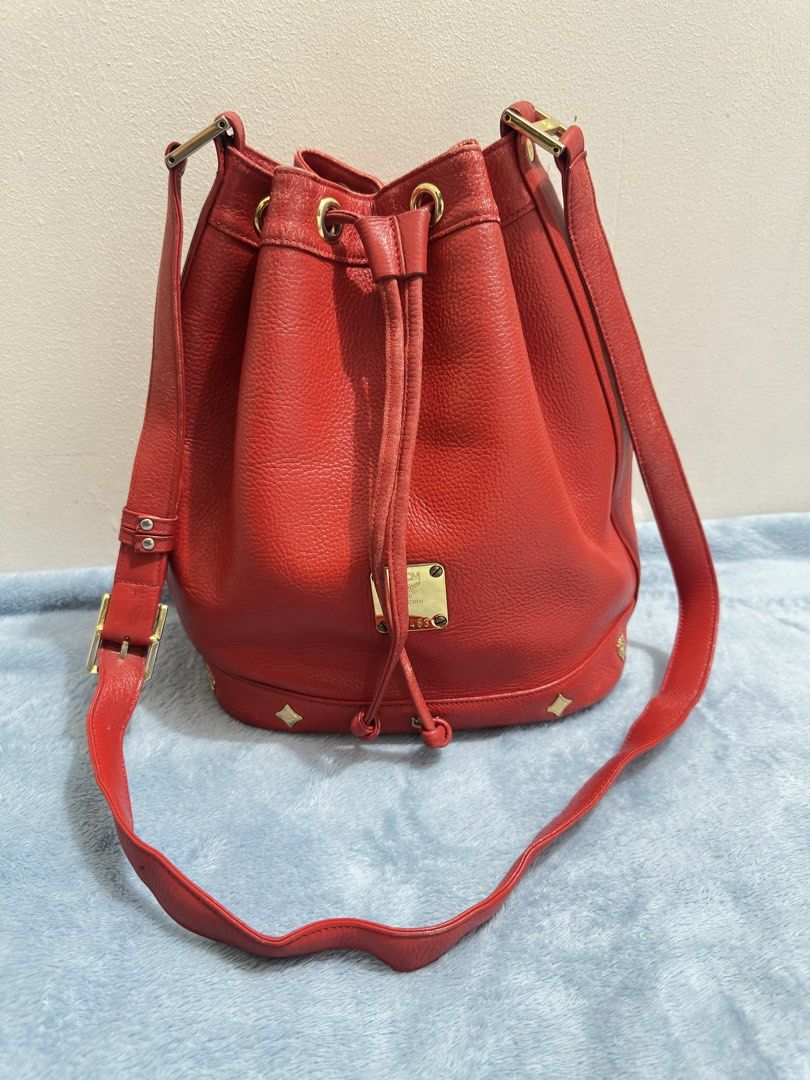 MCM Red vintage Leather Bucket Bag (Category: Tote Bags) located in Calamba. Submitted by nympha0630 (Listing ID 1467876289, Image 1). Description: - Authentic MCM bucket bag in a striking bright red pebbled leather - Features secure drawstring closure and shiny gold-tone hardware with front logo plate - Adjustable shoulder strap for comfortable wear - Bottom equipped with four protective metal feet and stylish diamond hardware - Condition: Sligh
