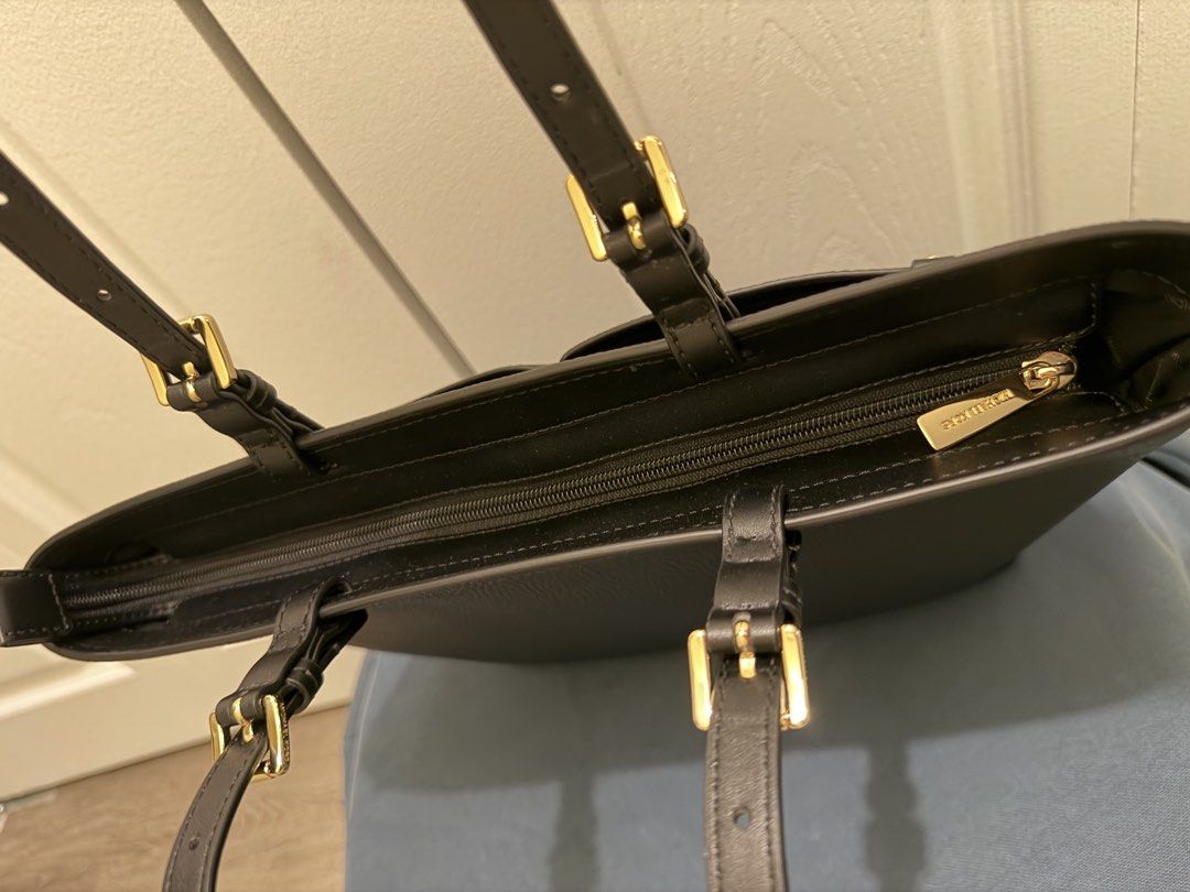 Michael Kors Black Jet Set Medium Pocket Tote Bag (Category: Tote Bags) located in Tabuk. Submitted by farawayluxe (Listing ID 1468005149, Image 3). Description: Black pebble leather tote bag from Michael Kors with gold-tone hardware. Double shoulder straps with adjustable buckle details. Front features two open slip pockets and gold metal lettering. Main compartment zips closed. Interior lined with dark patterned fabric and branding throughout. 